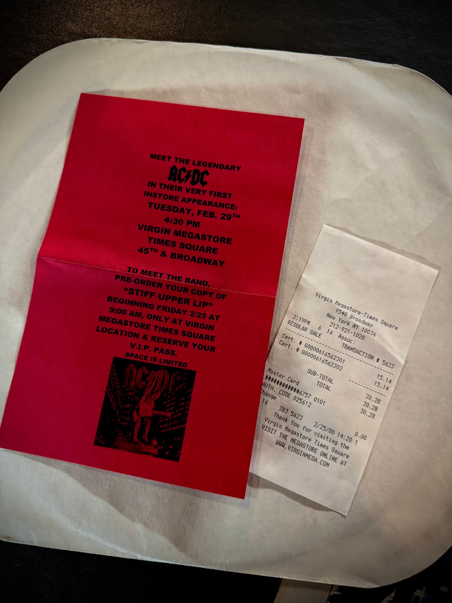 Red promotional flyer for AC/DC concert on a white surface with a receipt.