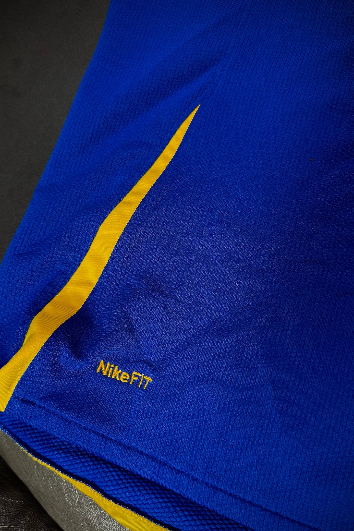 Blue athletic shirt with yellow stripe and 'NikeFIT' logo on a dark background