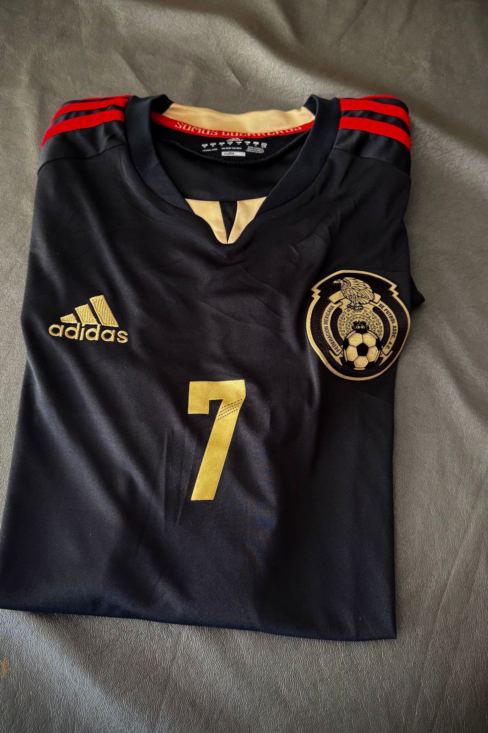 Black soccer jersey with gold number 7 and Adidas logo on a gray surface