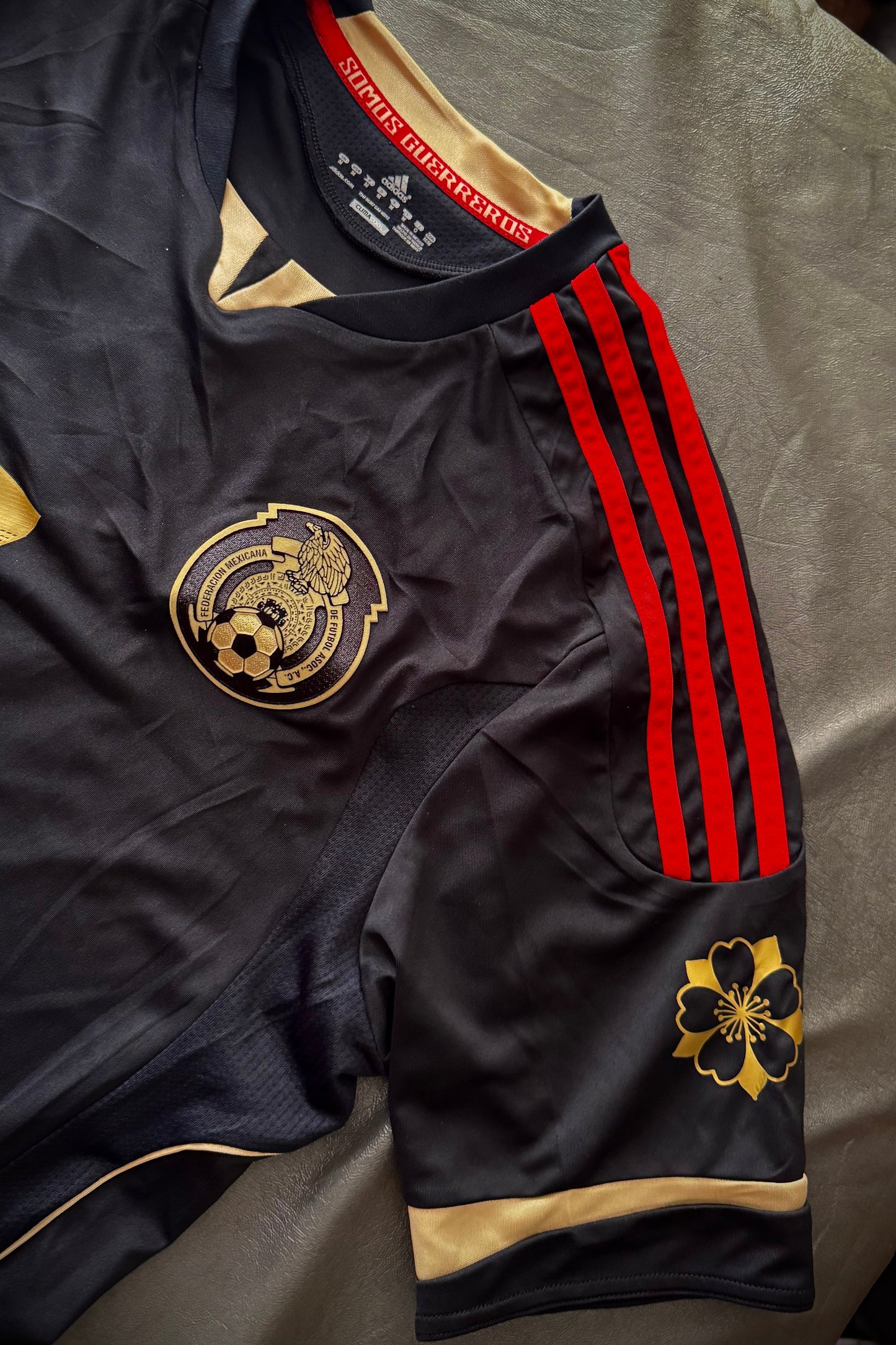 Black sports jersey with red stripes and gold logos on a gray surface