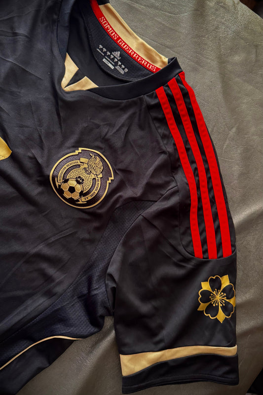 Black sports jersey with red stripes and gold logos on a gray surface