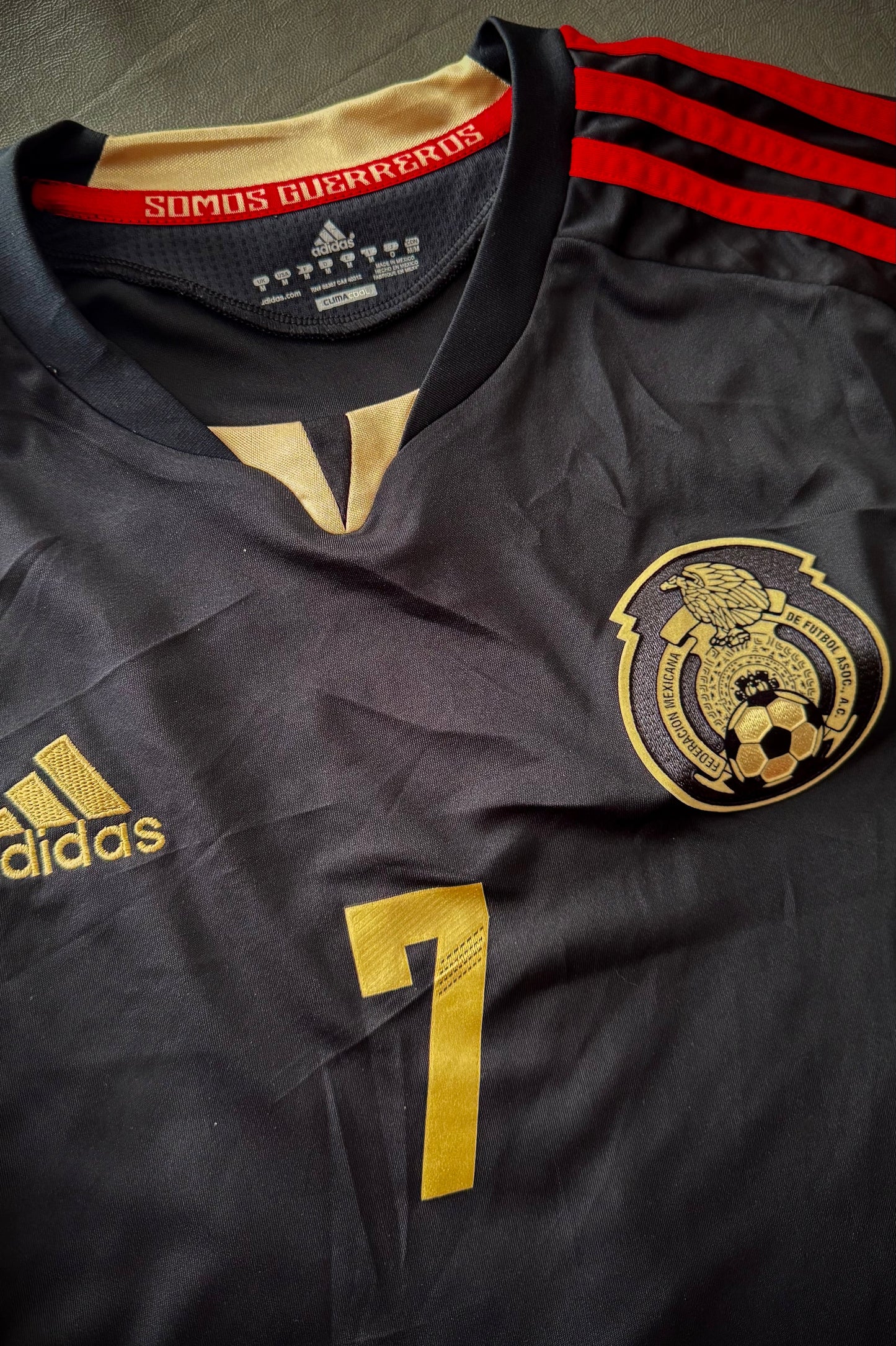 Black sports jersey with gold and red details, featuring Adidas logo and a club emblem.