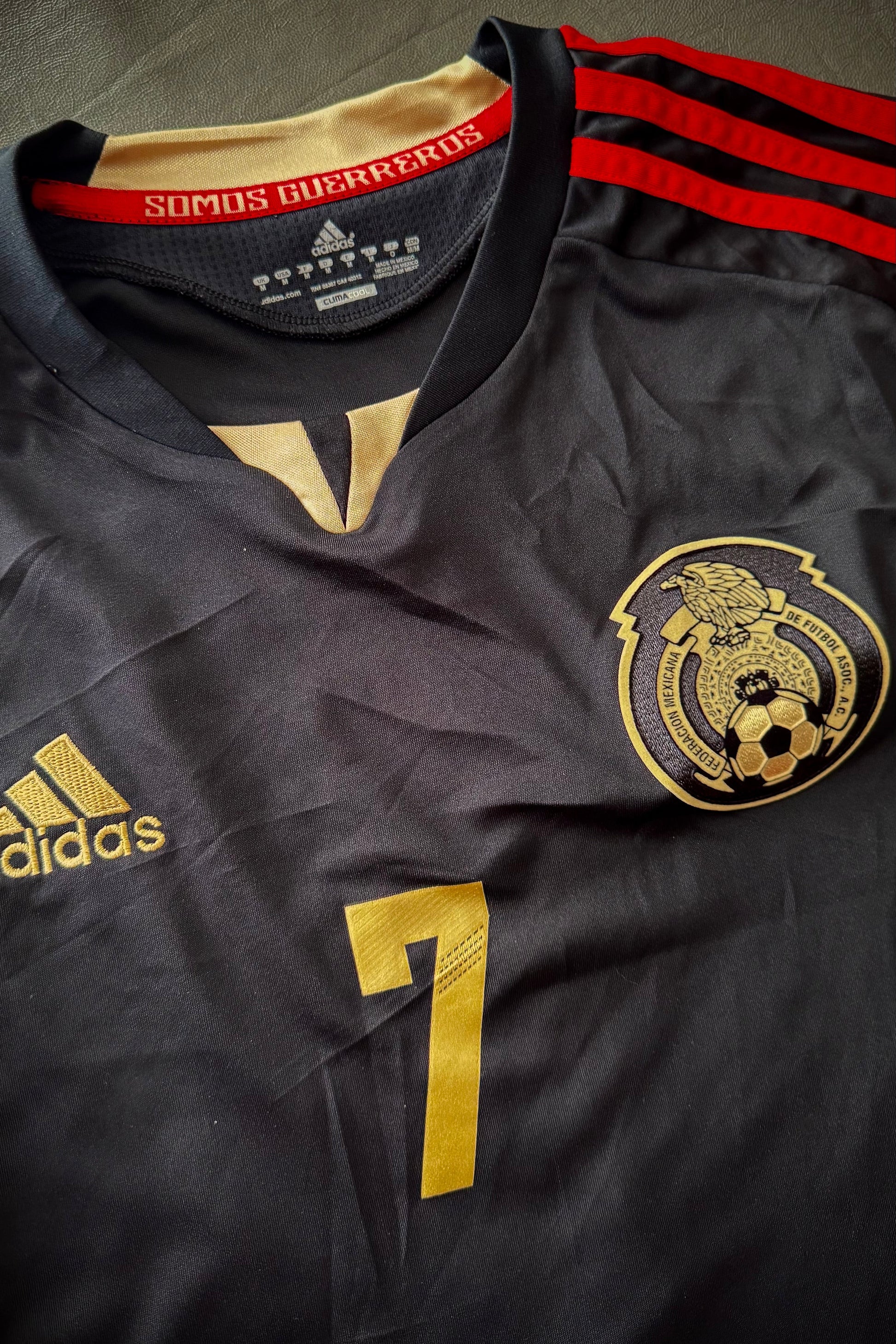 Black sports jersey with gold and red details, featuring Adidas logo and a club emblem.