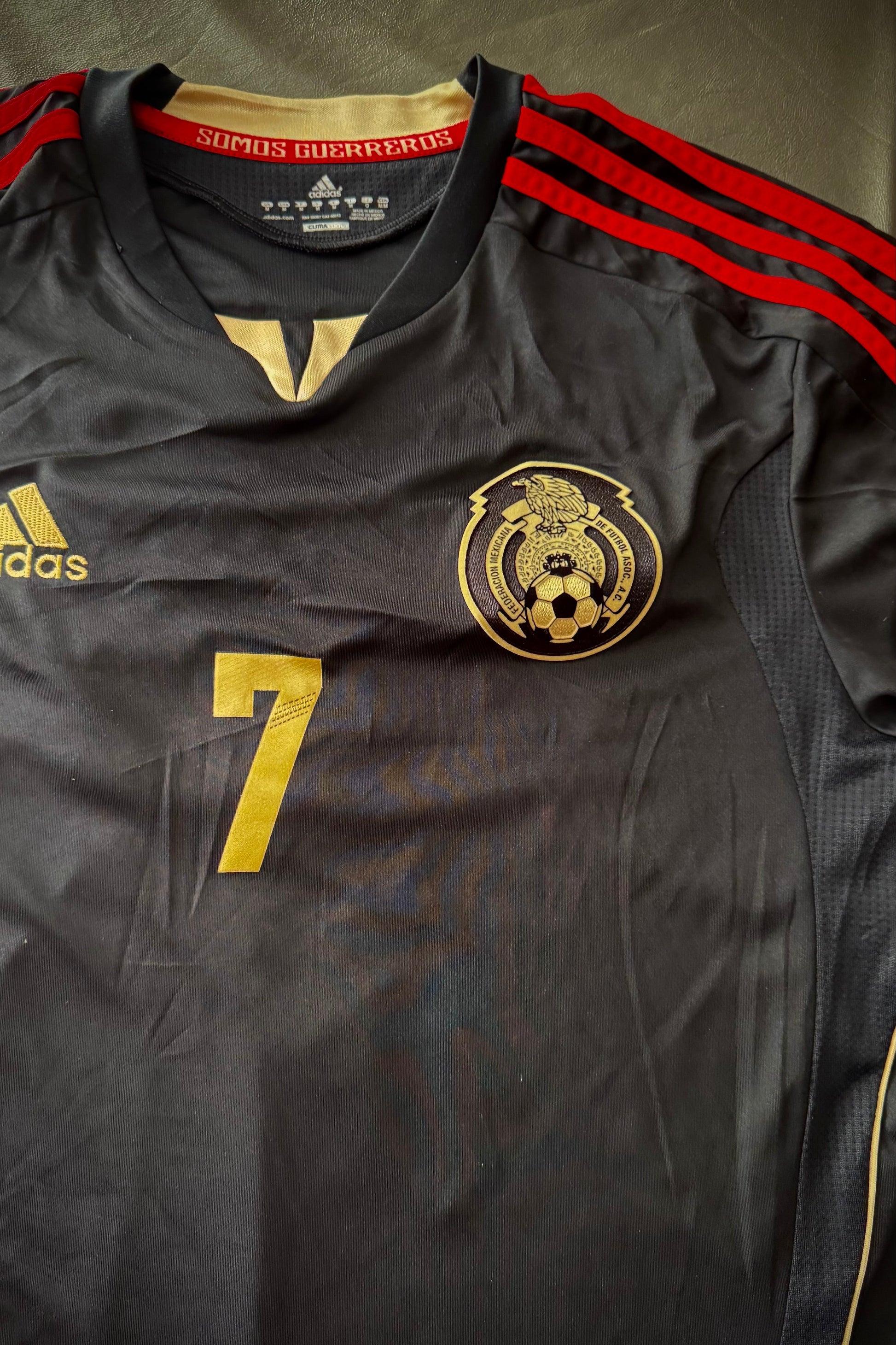 Black sports jersey with red stripes, Adidas logo, and number 7 on a dark background