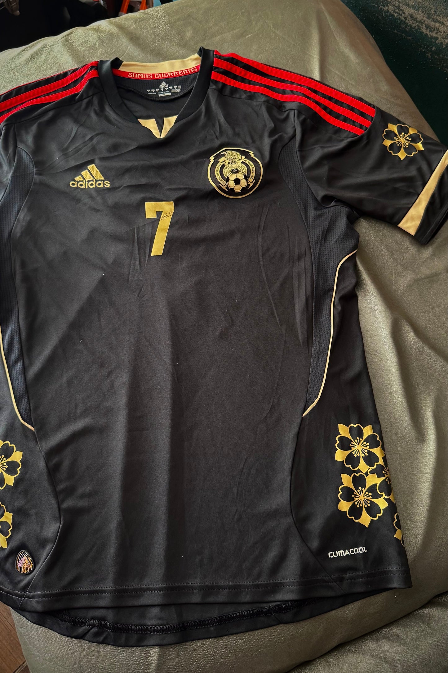 Black sports jersey with red stripes on shoulders, number 7, and Adidas logo, laid flat on a surface.