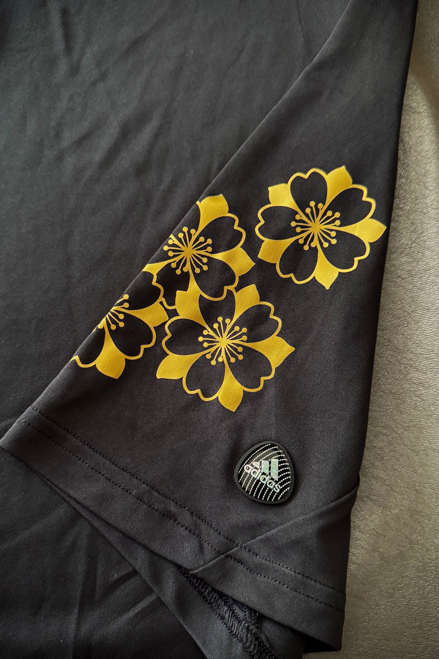 Dark fabric with yellow floral patterns and a small logo on a neutral background