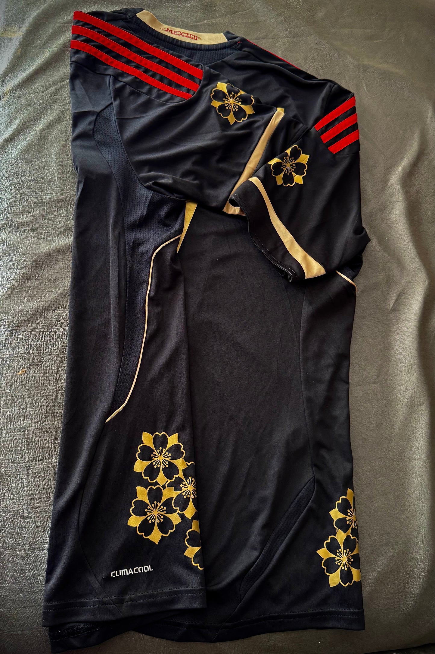 Black sports jersey with red stripes and gold patterns on a gray surface