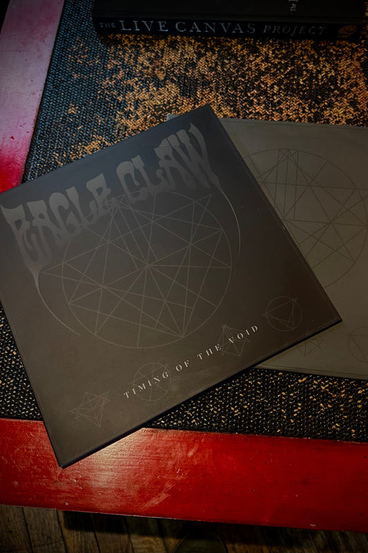 A vinyl record of Eagle Claw titled 'Timing Of The Void' with a clear and black splatter design, placed on a red surface.