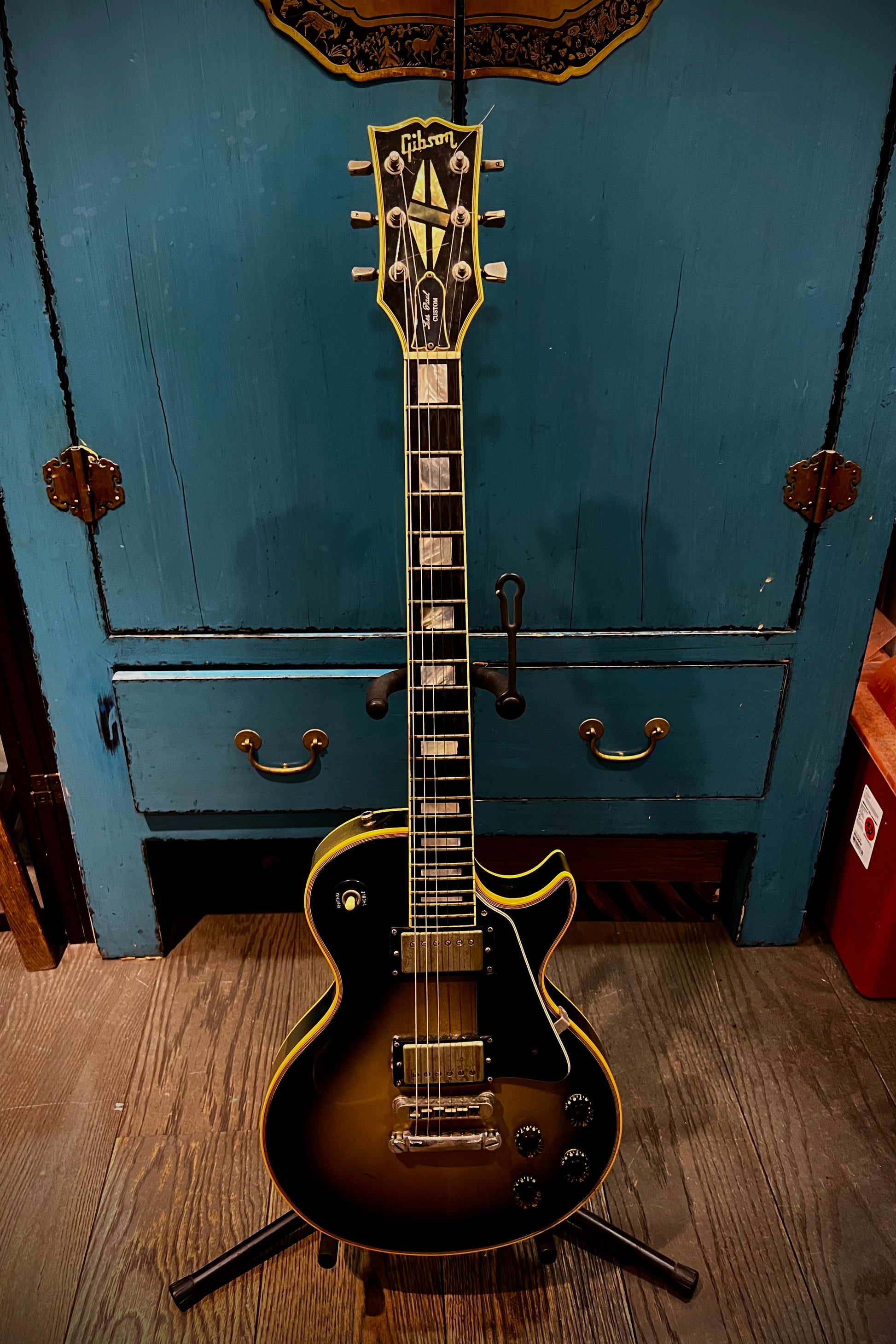 Electric guitar on a stand against a blue cabinet with gold handles.