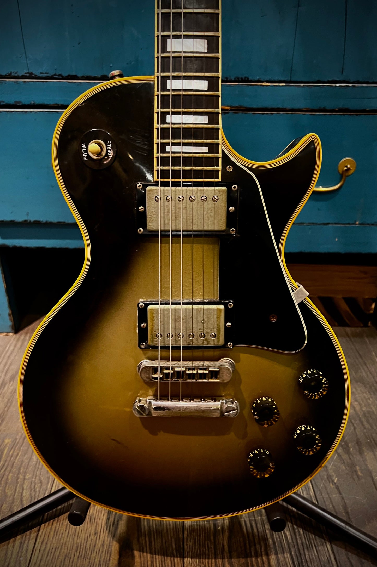 Electric guitar with a sunburst finish on a stand against a blue wooden background