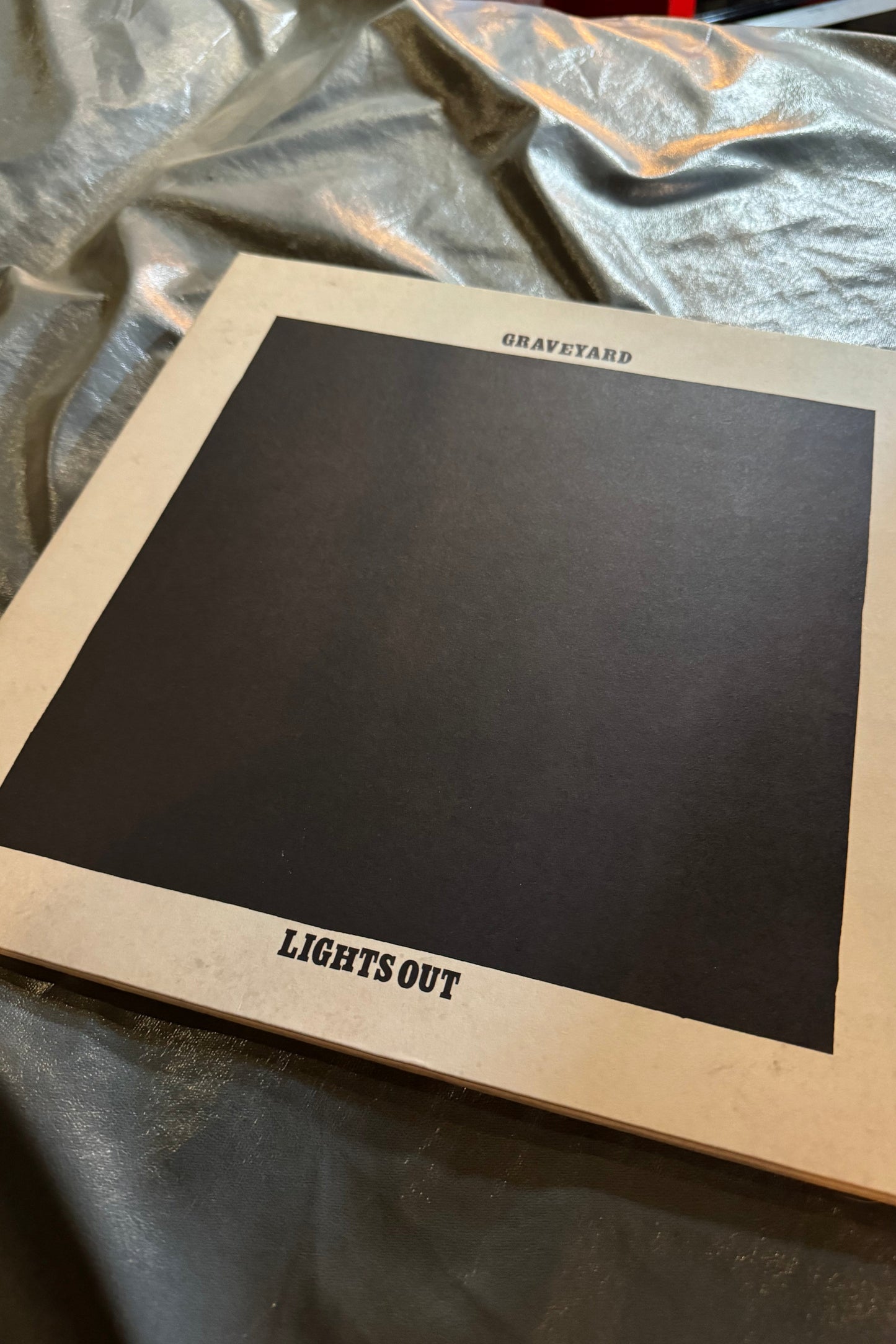 A vinyl record titled 'Graveyard Lights Out' with an orange vinyl color edition, displayed on a surface with a checkered pattern.