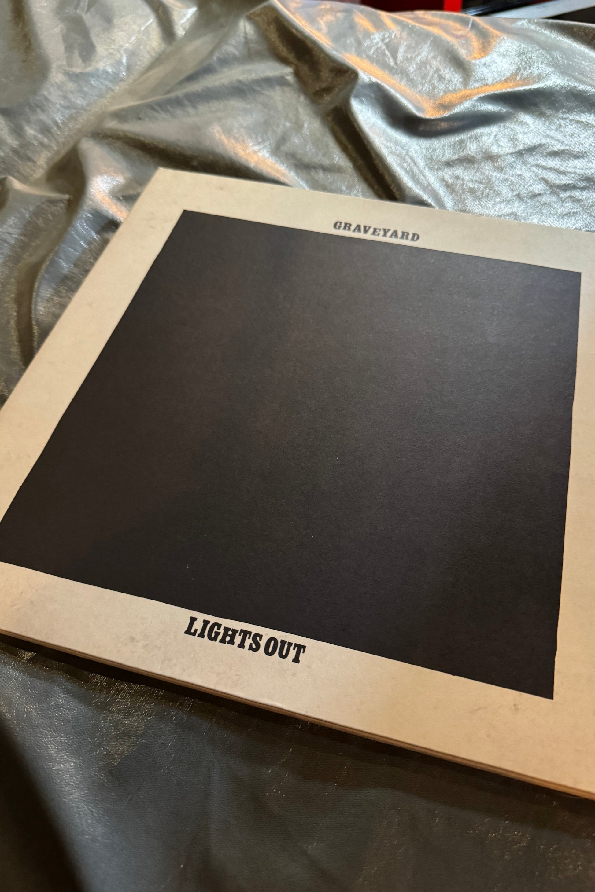 A vinyl record titled 'Graveyard Lights Out' with an orange vinyl color edition, displayed on a surface with a checkered pattern.