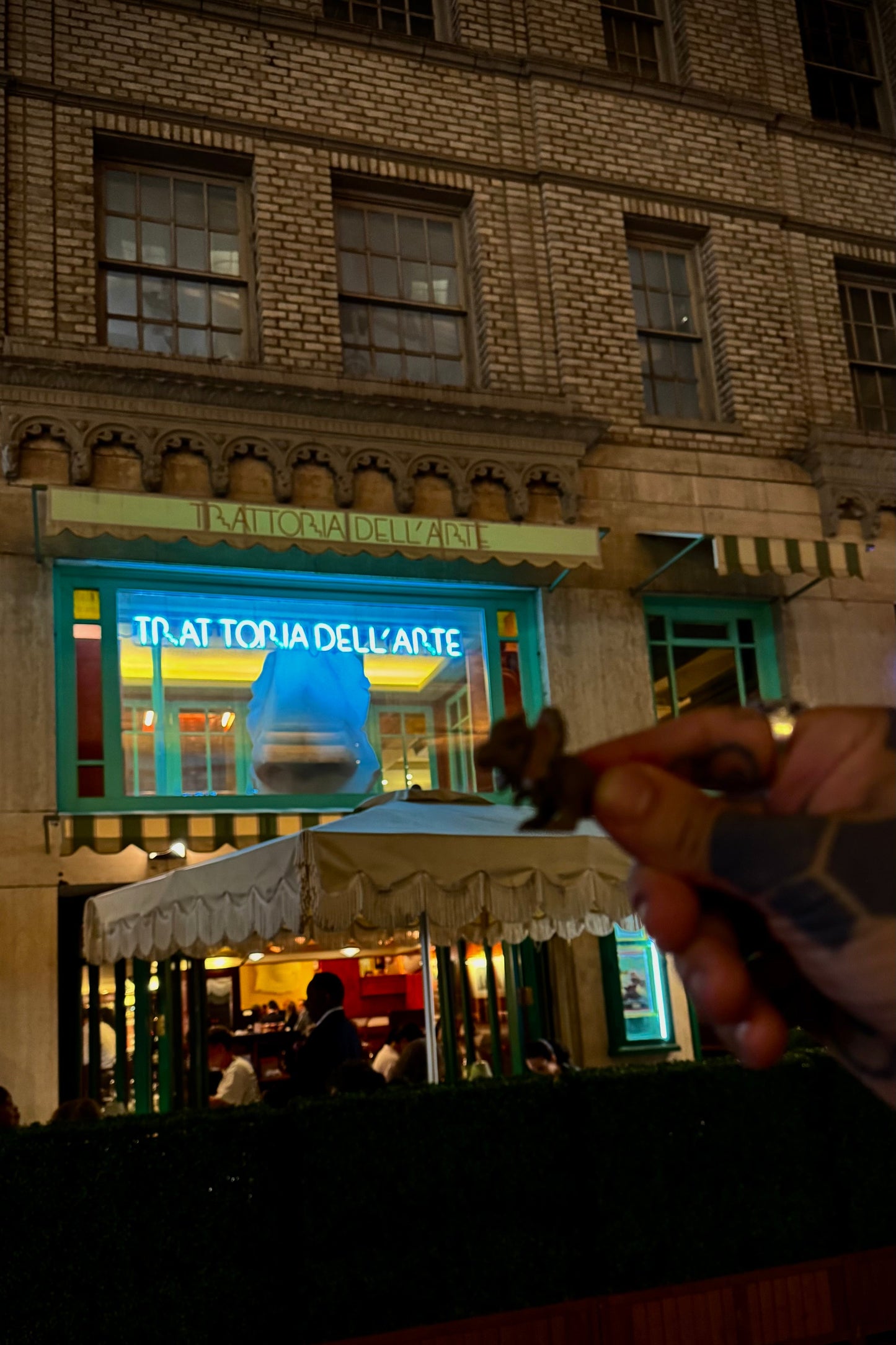Person holding a small object in front of a restaurant at night