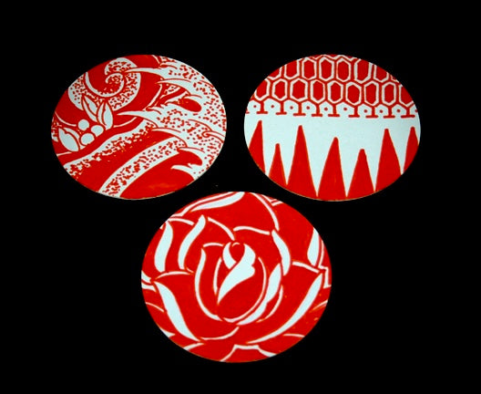 Three round paper coasters with red and white decorative patterns, displayed against a black background.