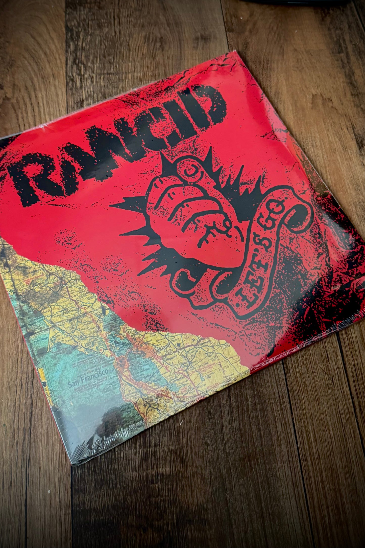 A vinyl record of Rancid's album 'Let's Go' with a red cover featuring the band's name and logo, placed on a wooden surface.