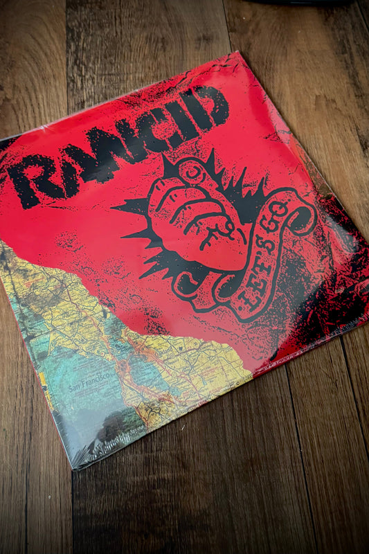 A vinyl record of Rancid's album 'Let's Go' with a red cover featuring the band's name and logo, placed on a wooden surface.