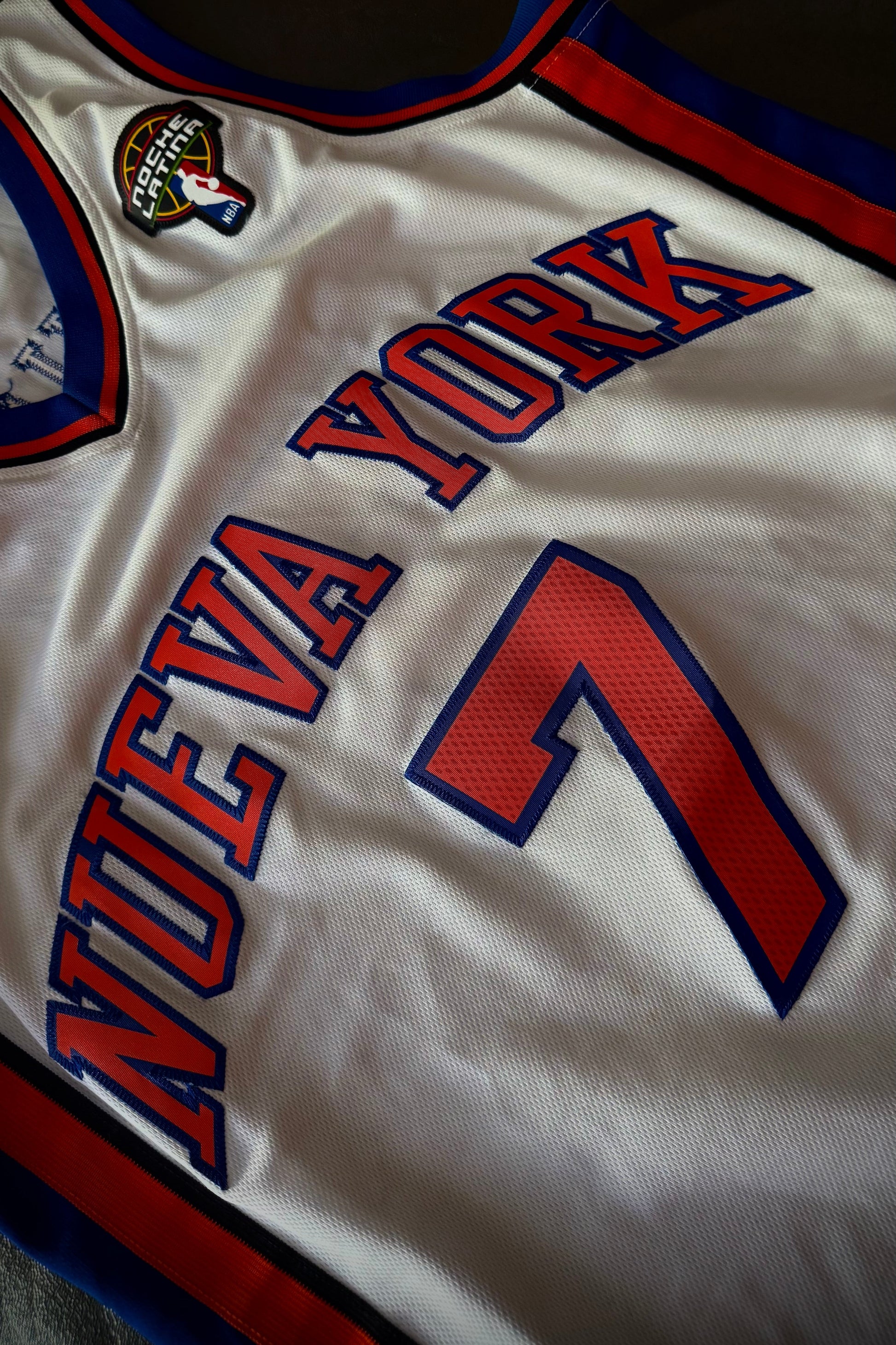 White sports jersey with red and blue text and numbers on a dark background