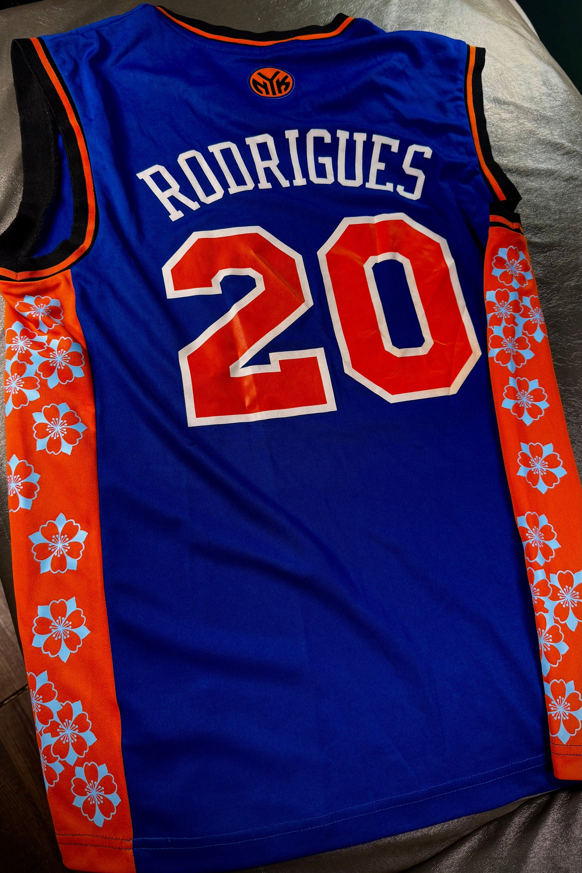 Blue basketball jersey with orange accents and 'RODRIGUES 20' printed on a bed