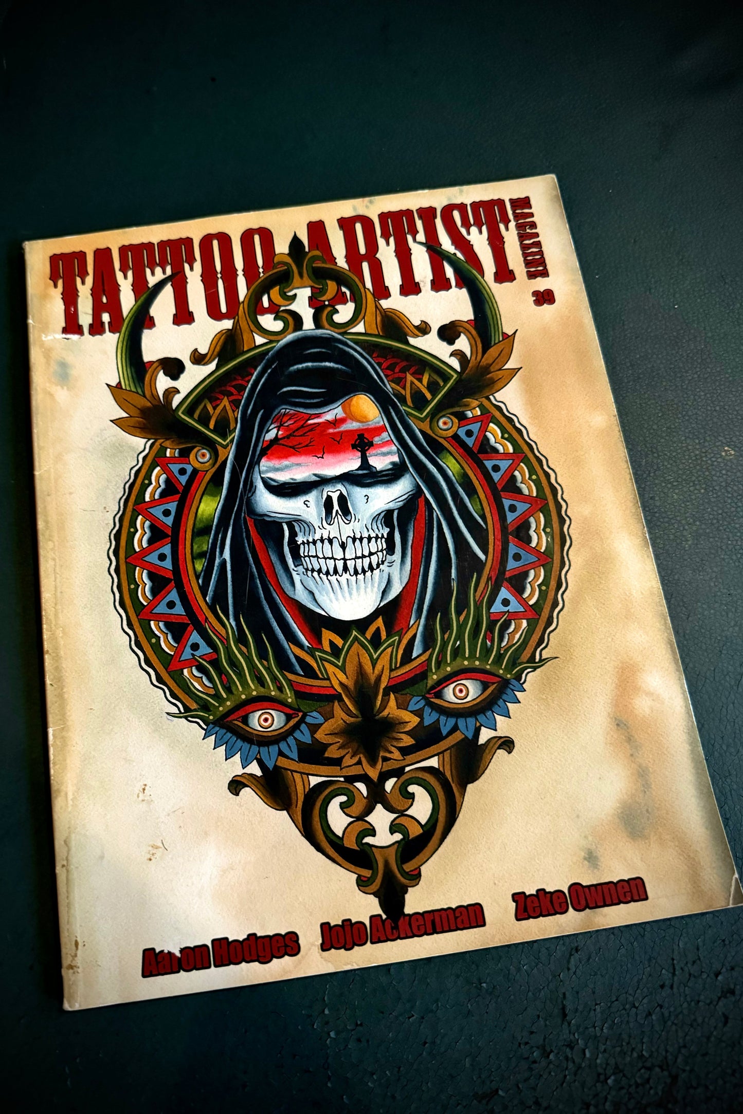 A cover of 'Tattoo Artist' magazine featuring a colorful illustration of a skull with ornamental designs.