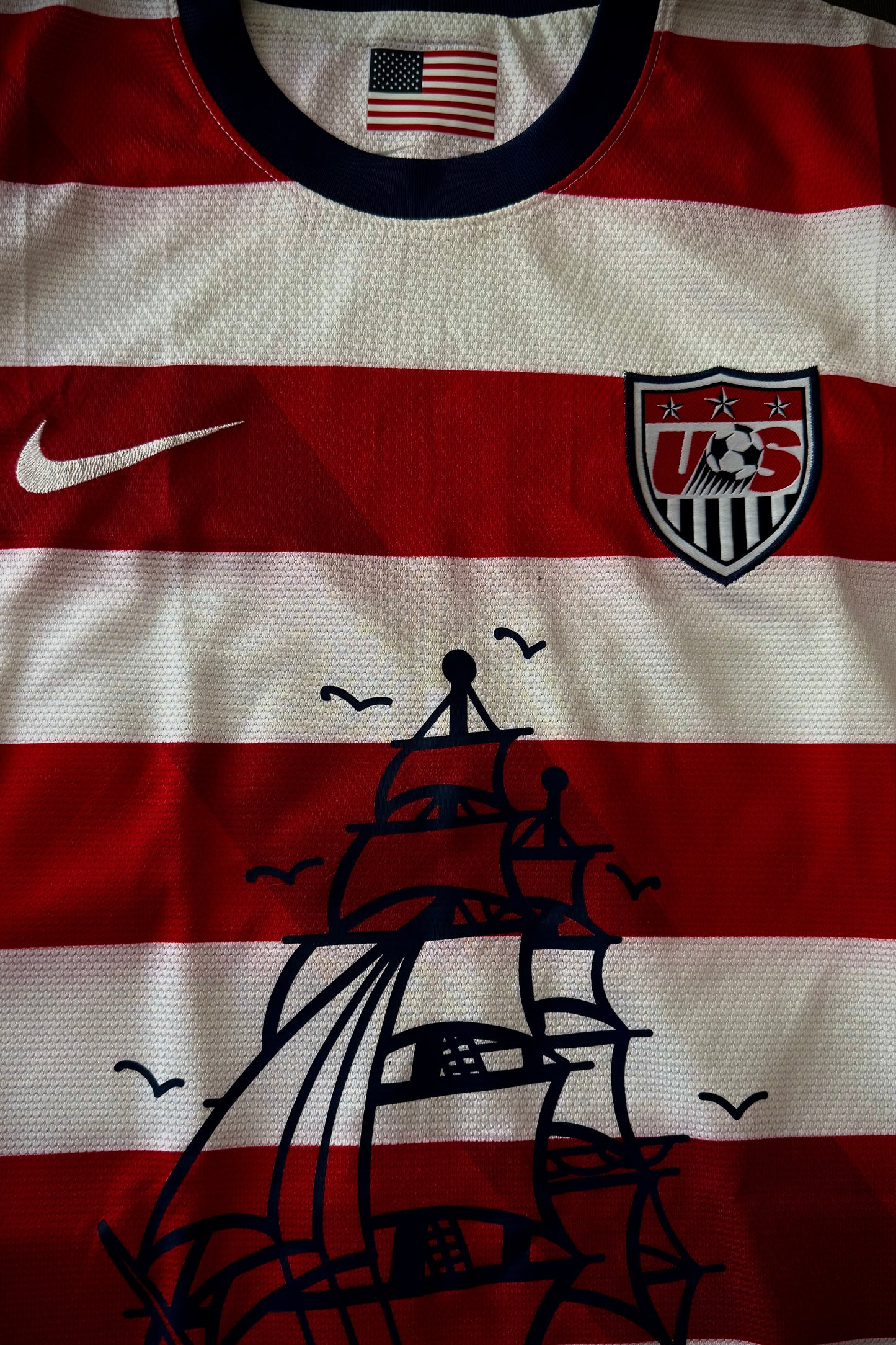 Sports jersey with American flag, Nike logo, and ship design on a red and white striped background.