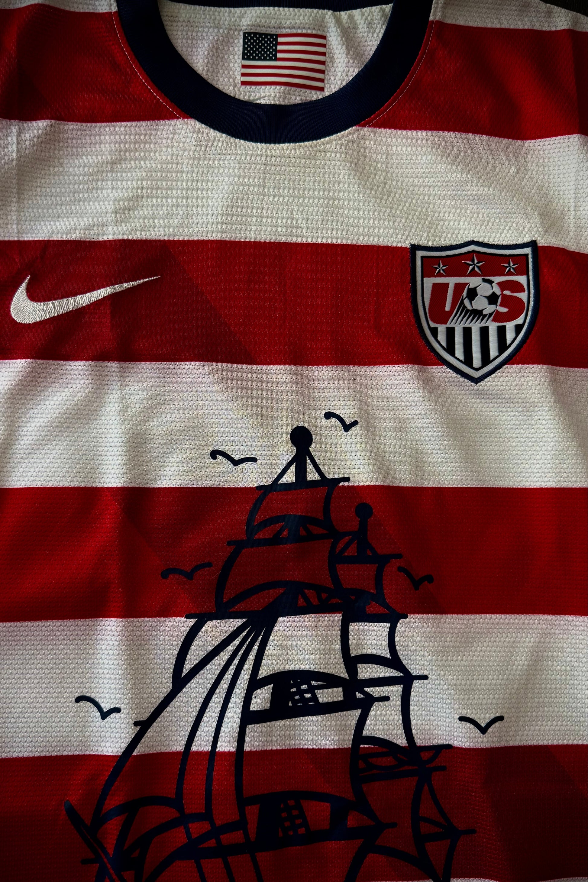 Sports jersey with American flag, Nike logo, and ship design on a red and white striped background.