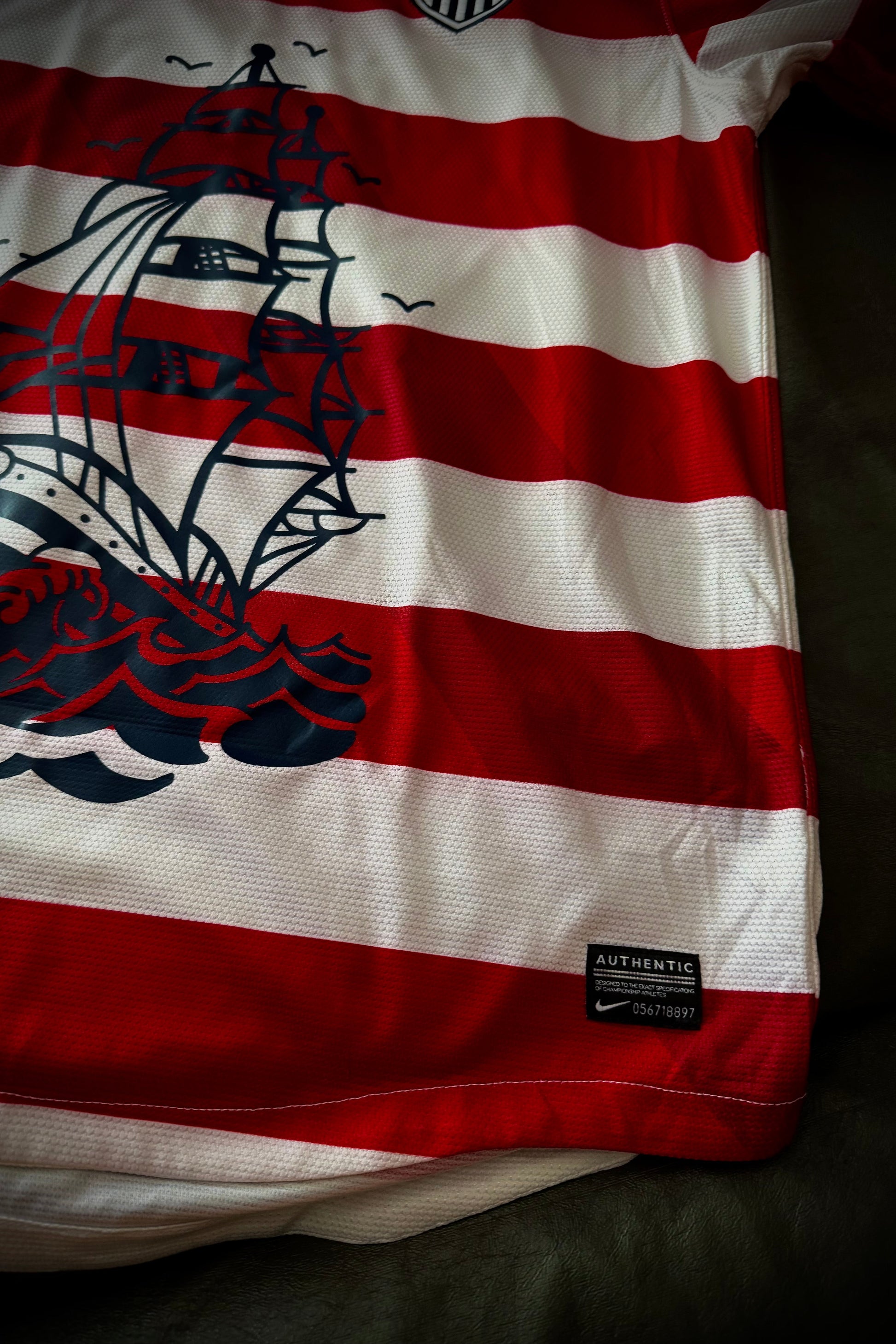 Red and white striped shirt with a ship design on a dark background