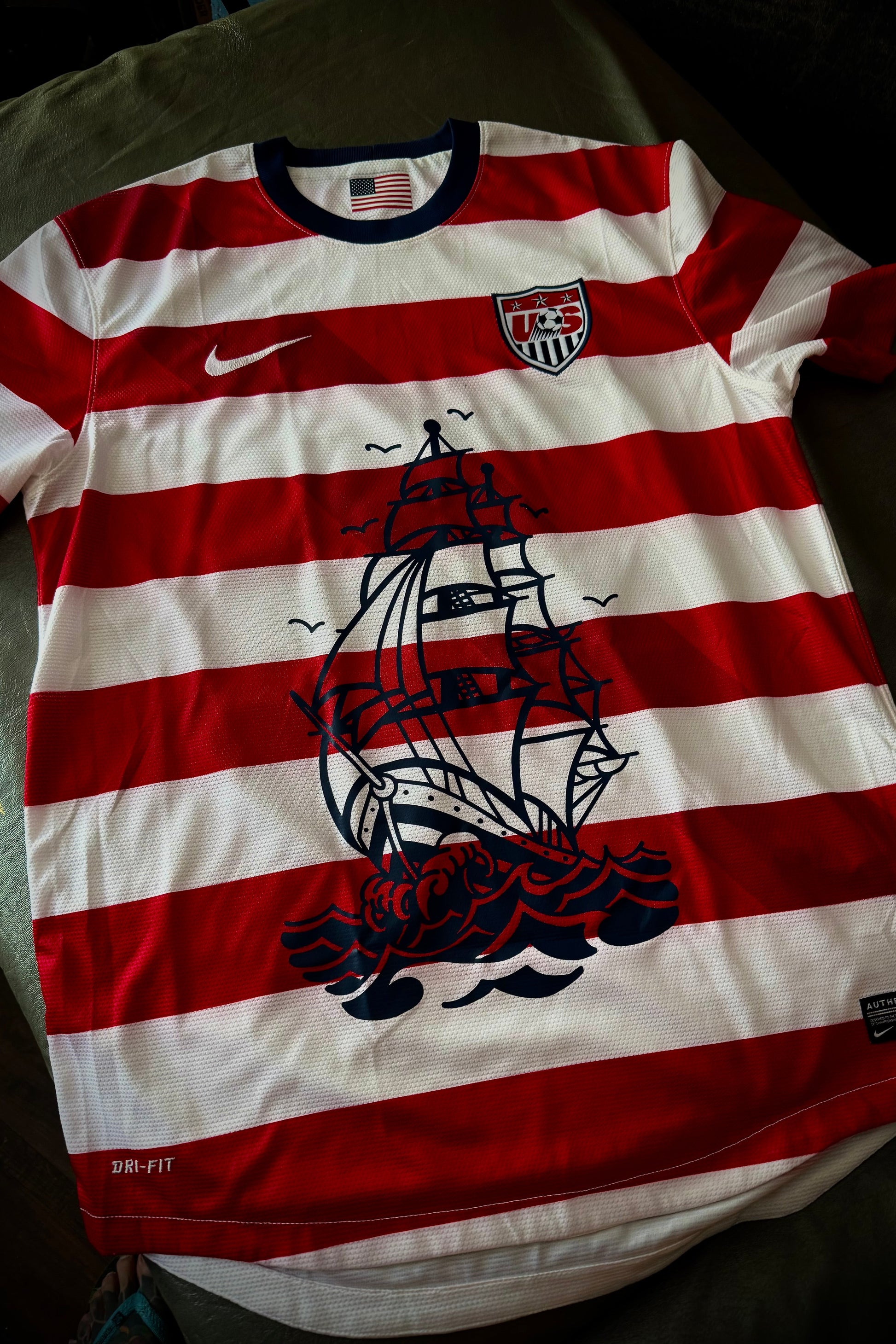 Red and white striped shirt with ship design and Nike logo on a dark surface