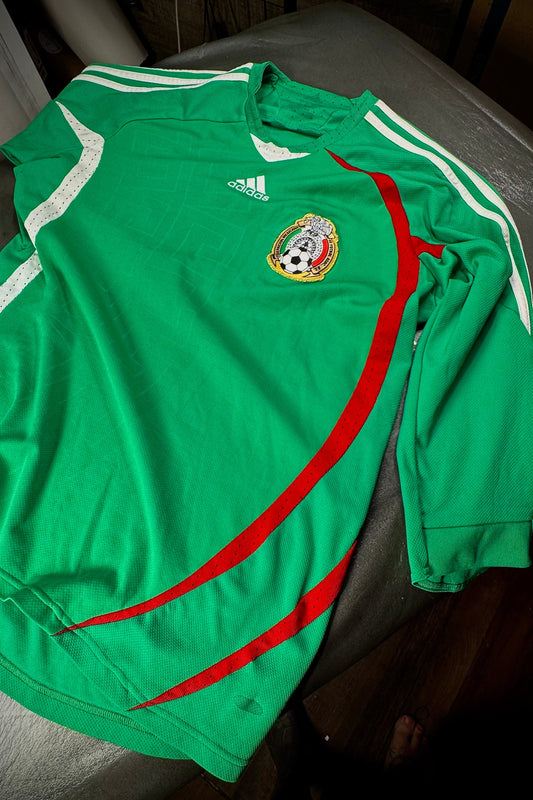 Green sports jersey with red accents and Adidas logo on a dark surface